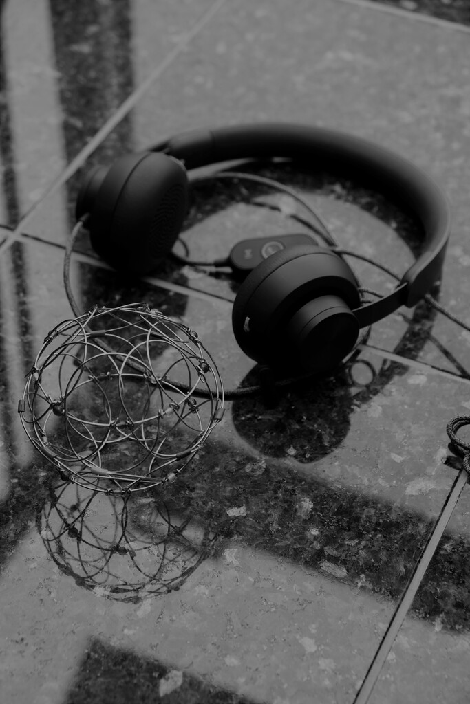 Auf grauem, marmoriertem Untergrund liegt das als Kugel geformte Faltmandala, das auch auf der Startseite sowie im Logo dargestellt ist. Es wird von einem schwarzen Headset umschlossen.
